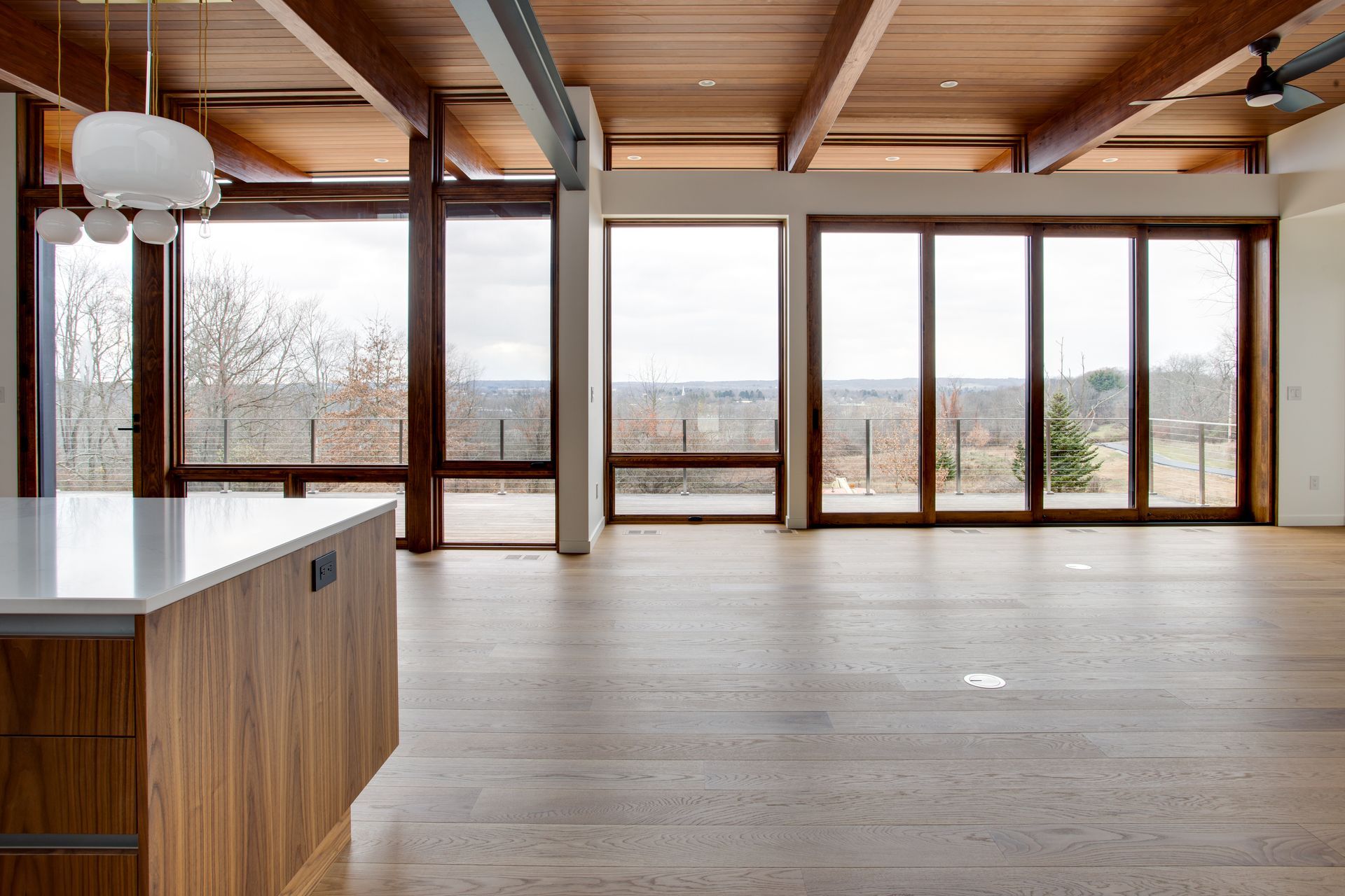 Modern open living room with wood floors, large windows, and a kitchen island, overlooking a snowy landscape