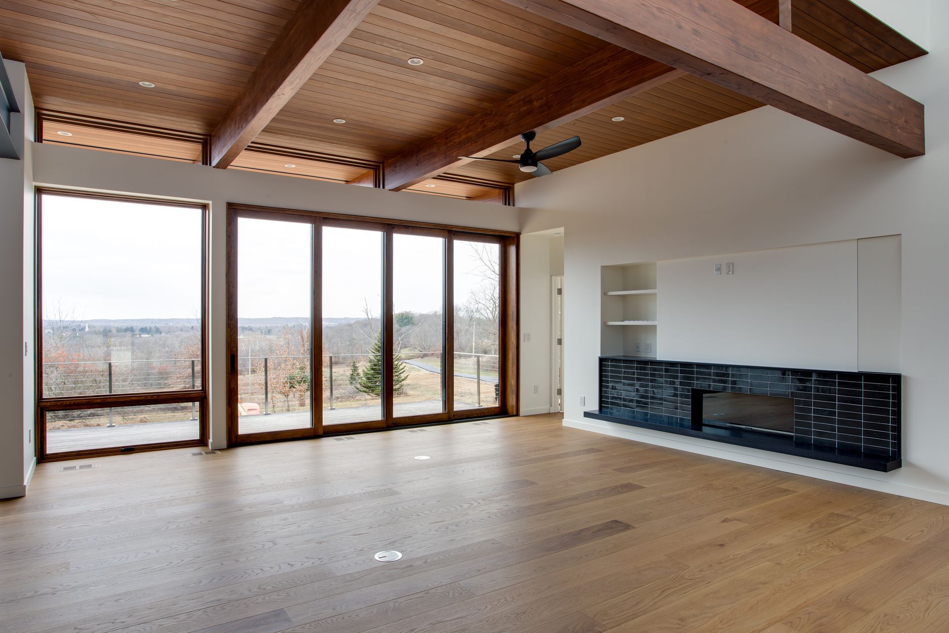 Spacious modern living room with wood ceiling, large windows, and a black fireplace mantel