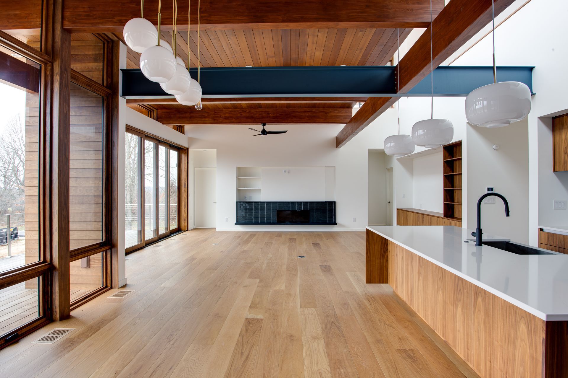 Spacious modern loft with wood floors, exposed beams, large windows, and a kitchen island with white countertops.