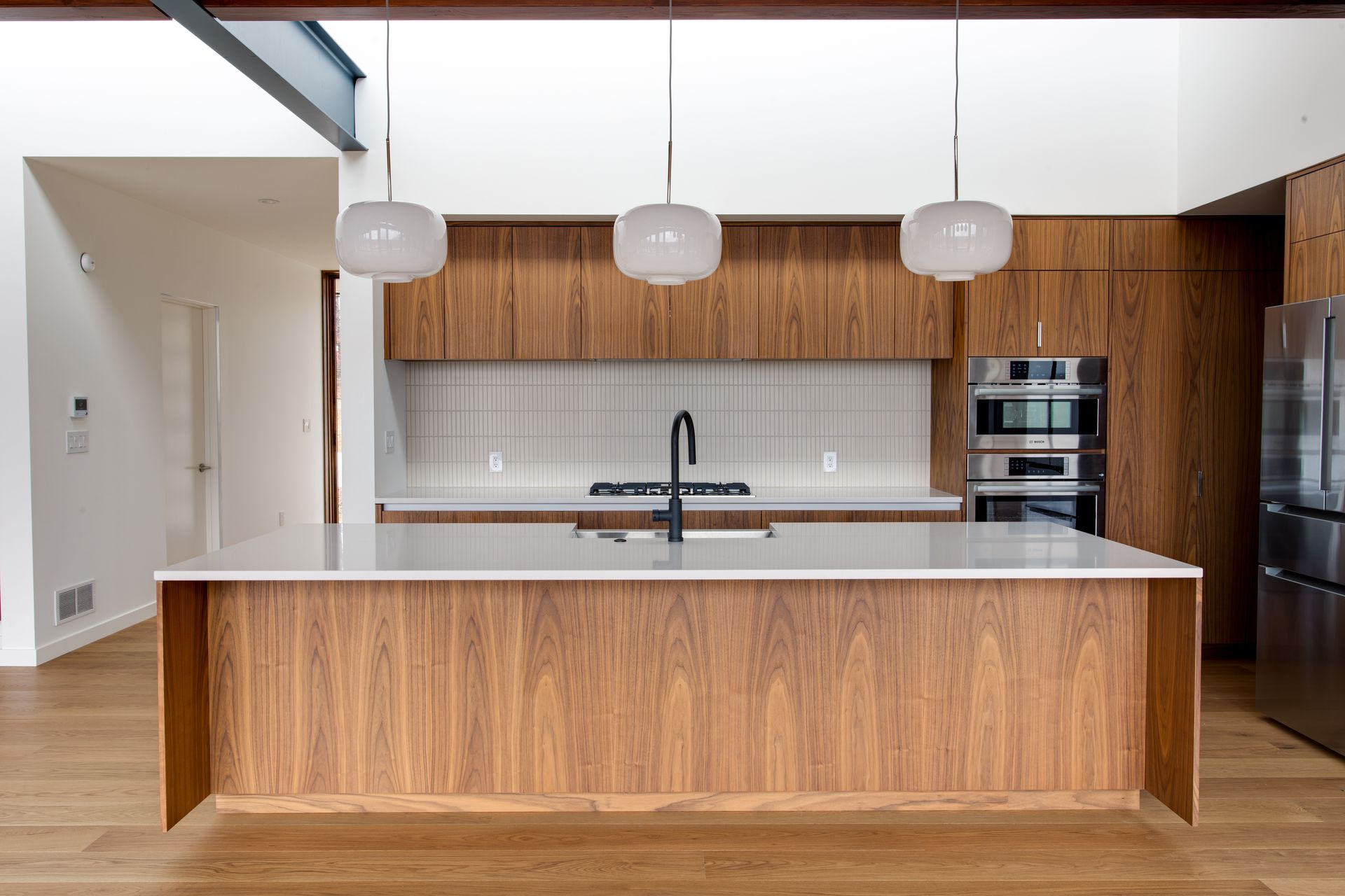 Modern kitchen with wood island, white countertops, pendant lights, and built-in oven cabinets