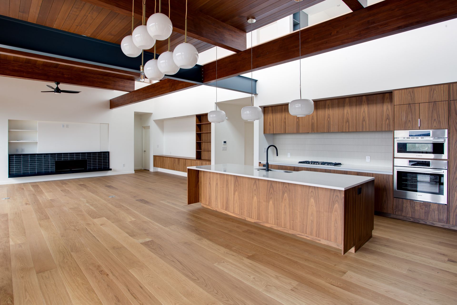 Modern kitchen with wood floors, vaulted ceiling, island, built-in ovens, and white pendant lights