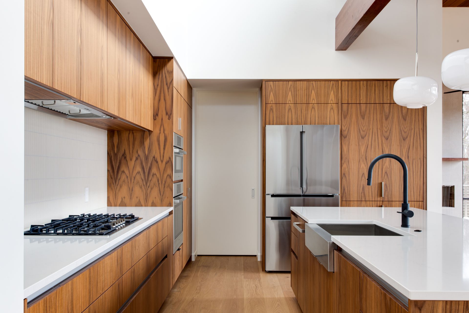 Modern kitchen with wood cabinets, white countertops, stainless steel fridge, and black faucet