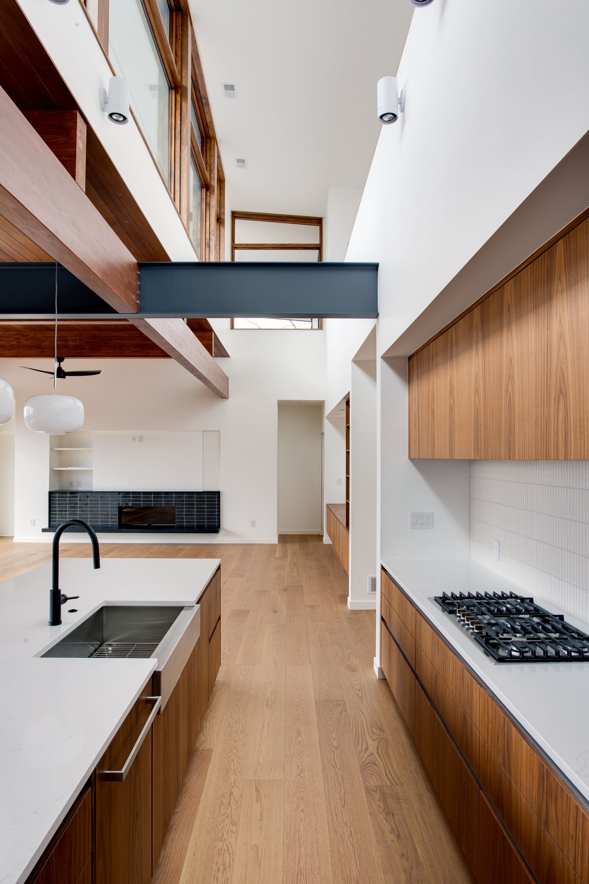 Modern kitchen with wood cabinetry, black countertops, white walls, and a high ceiling with exposed beams