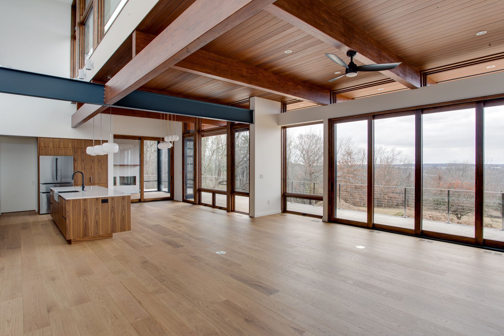 Spacious modern loft with wood floors, exposed beams, and large windows overlooking a snowy landscape