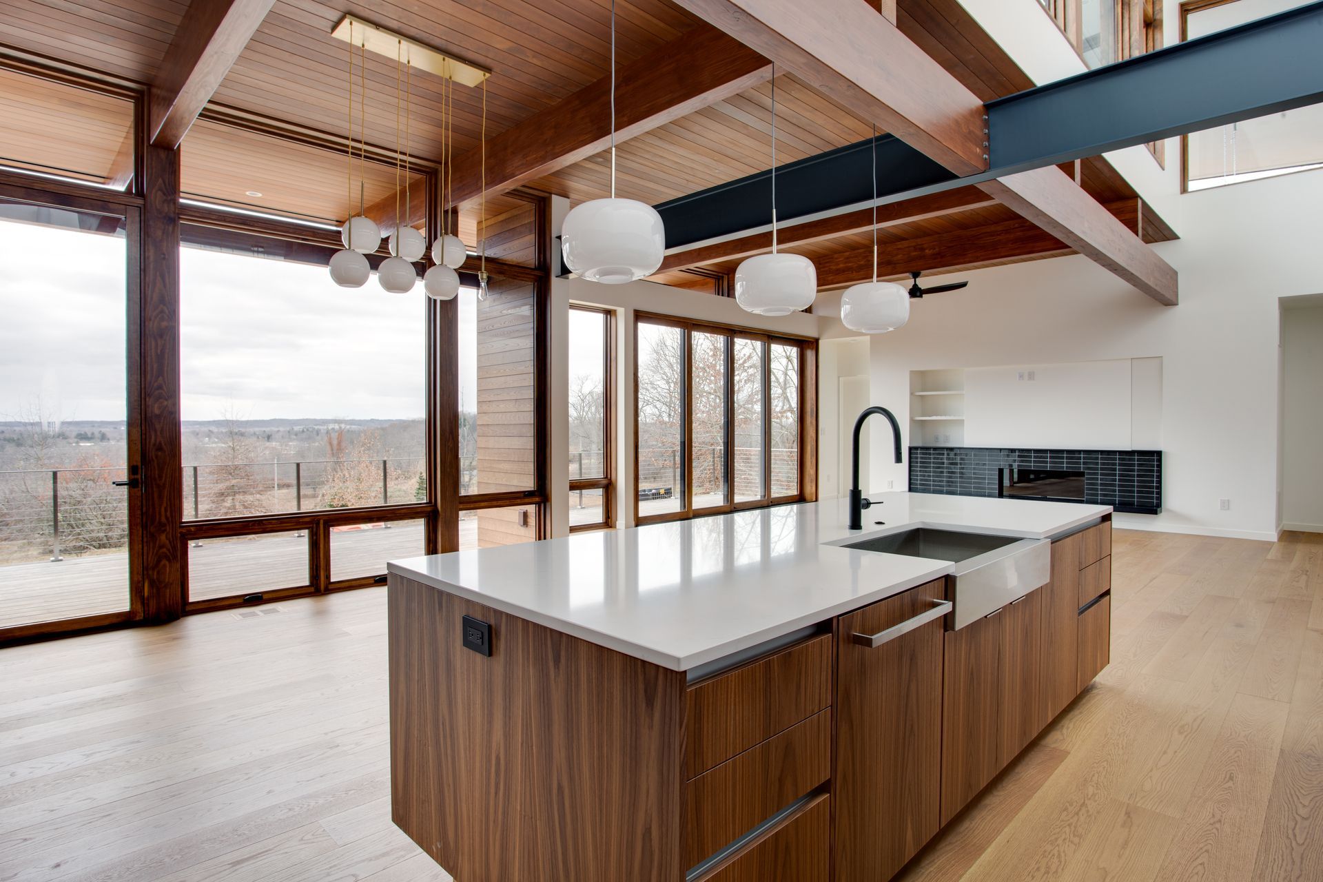 Modern open kitchen with wood beams, large windows, white island, and lakeside view