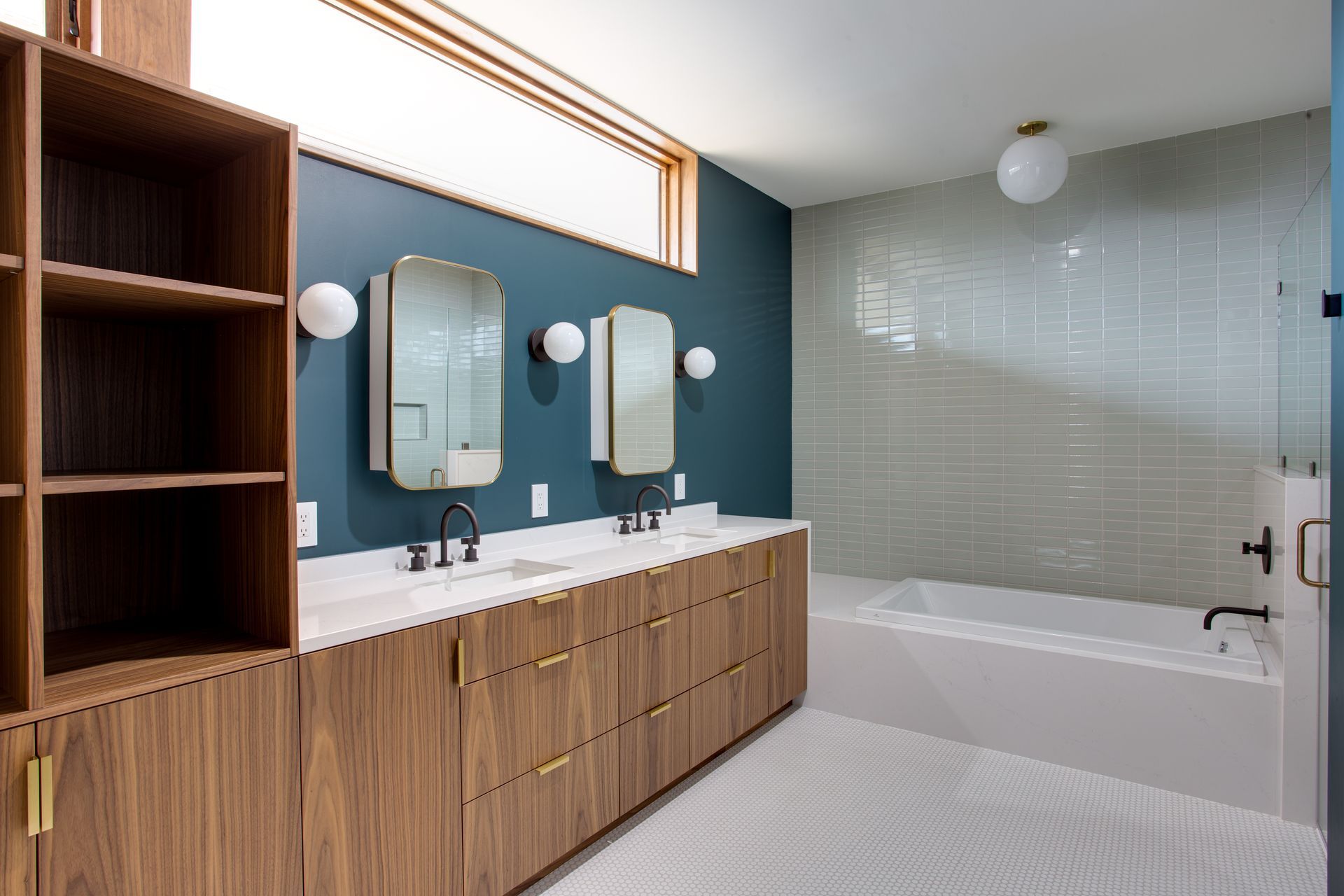 Modern bathroom with wooden vanity, blue accent wall, bathtub, and frosted glass shower area