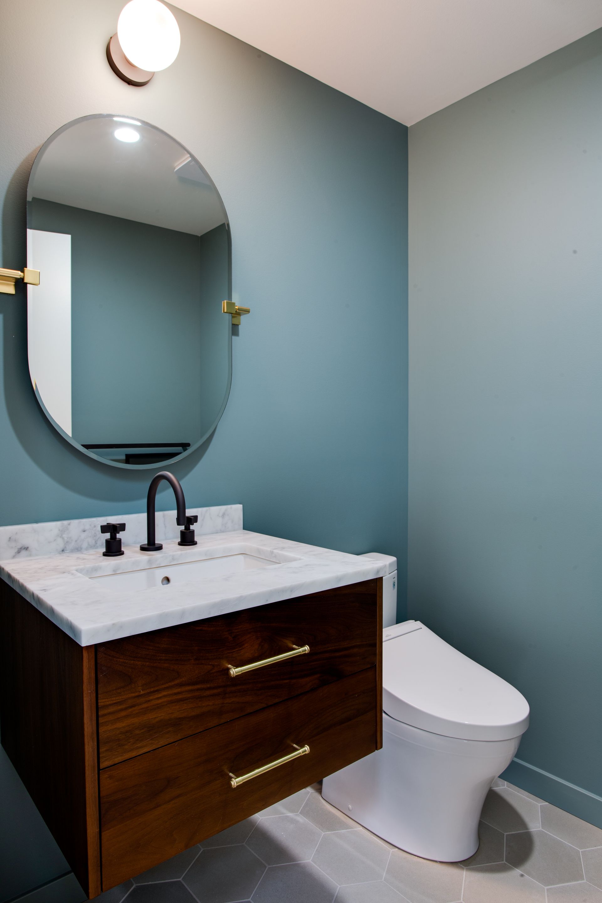 Bathroom with blue walls, white sink, oval mirror, and toilet beside a wood vanity.