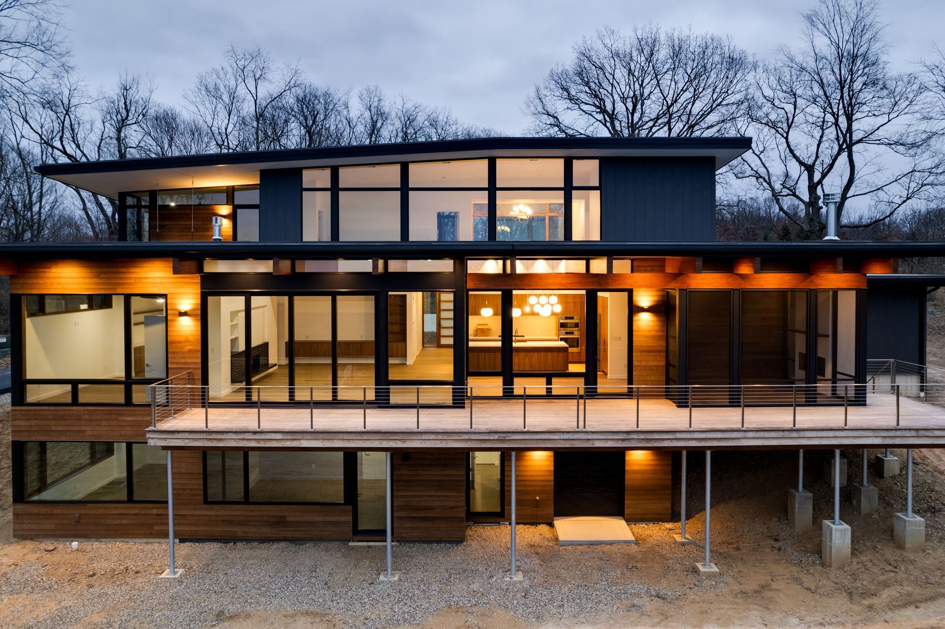 Modern two-story house with large glass windows and warm interior lights at dusk