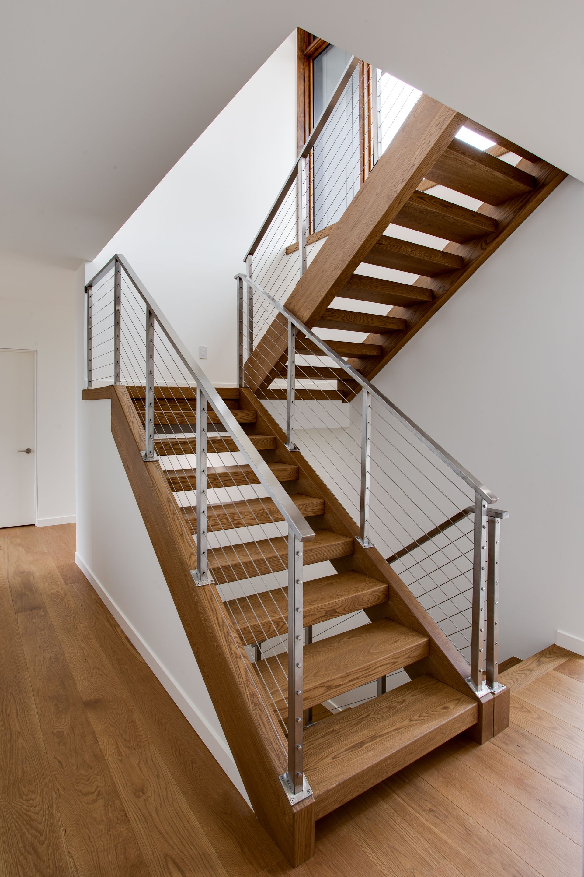 Wooden staircase with metal railings in a modern interior, ascending along a white wall