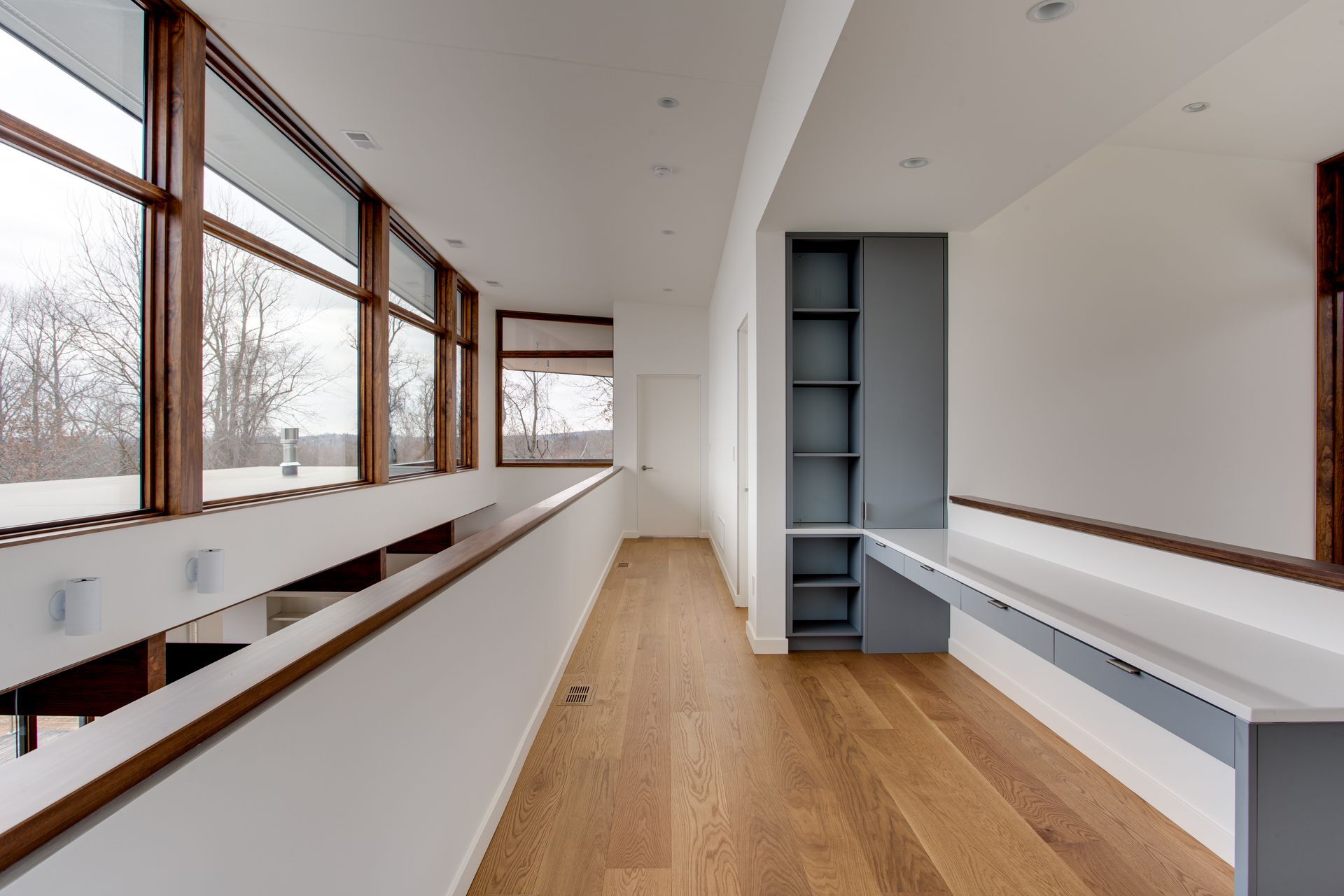 Bright modern hallway with wood floors, large windows, and built-in shelving on both sides