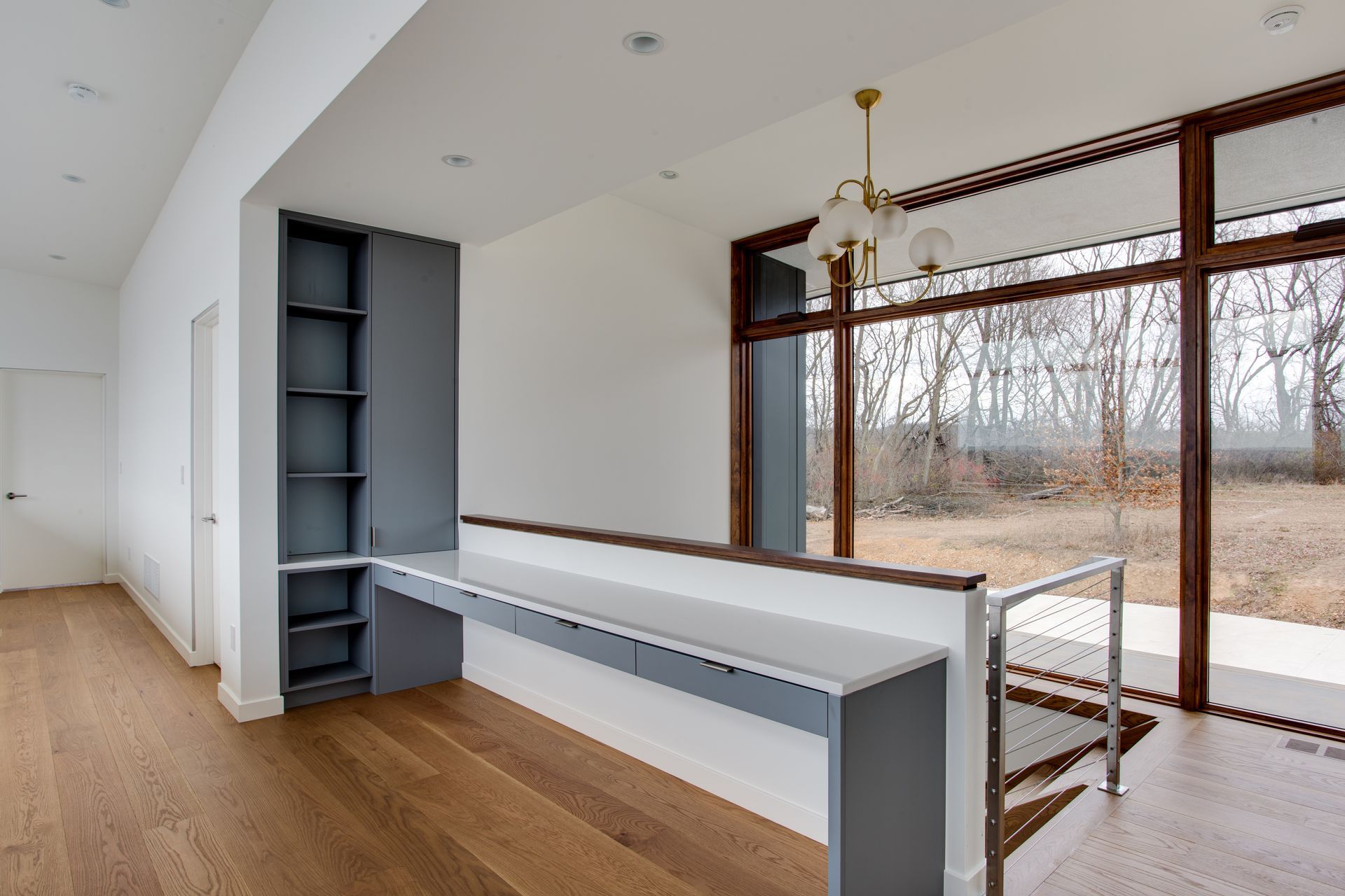 Modern open-plan room with built-in shelving, long counter, and large windows overlooking trees.