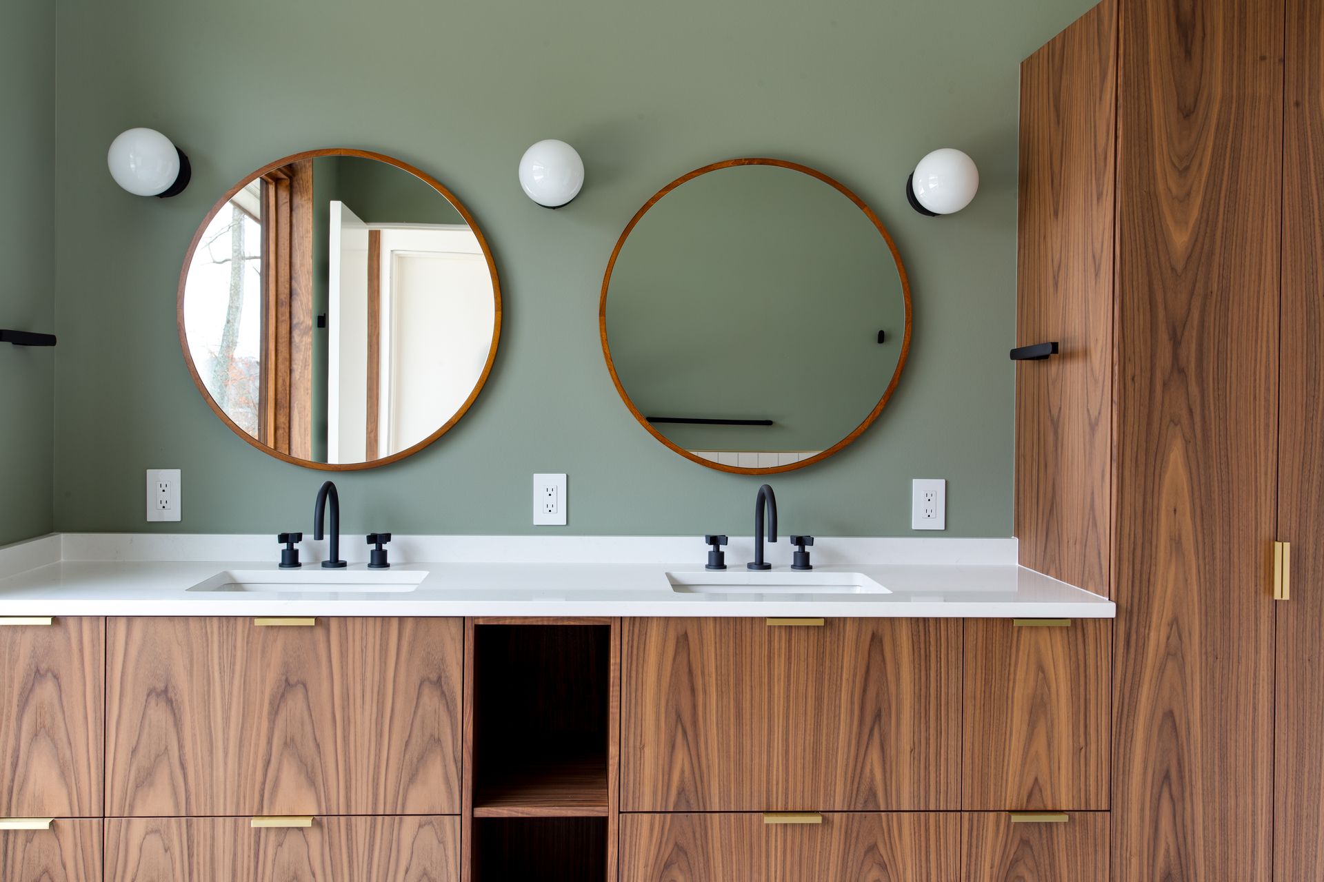 Modern bathroom vanity with two round mirrors, wood cabinets, white countertop, and sage green wall