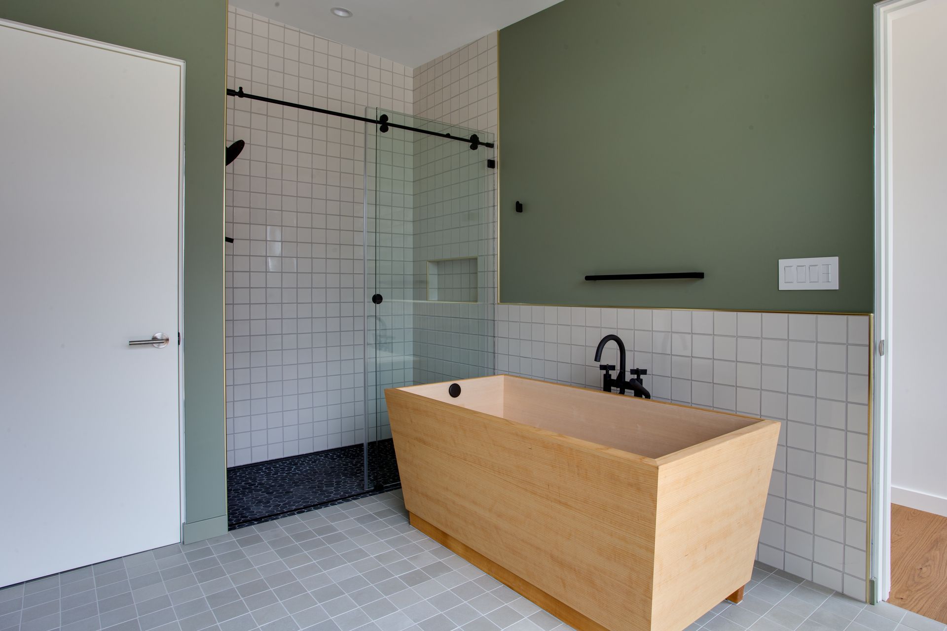 Modern bathroom with glass shower, wood tub, white tile, and green walls