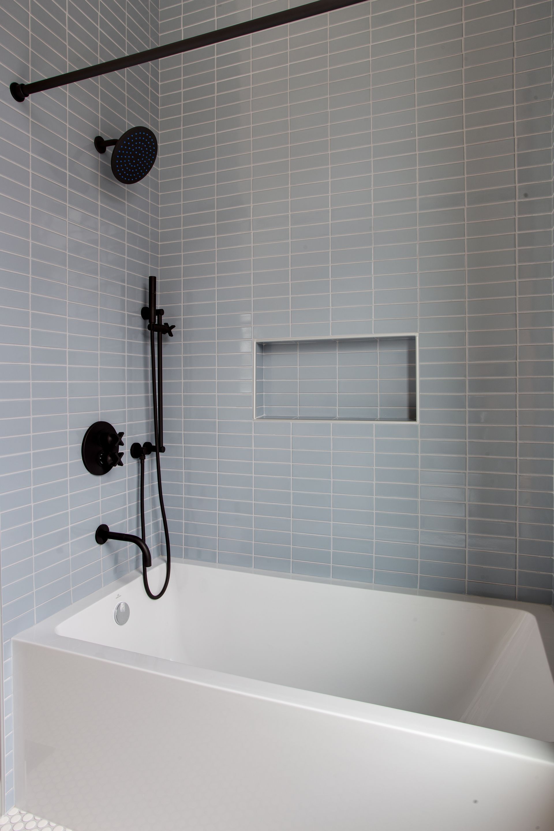 Modern white bathroom with black shower fixtures, tub, and tiled wall niche.