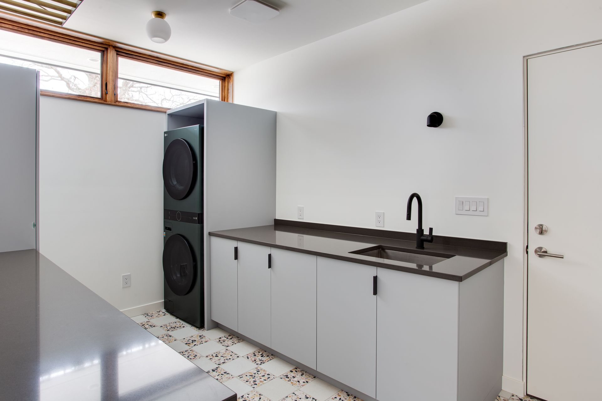 Laundry room with stacked washer and dryer, white cabinets, sink, and tile floor.