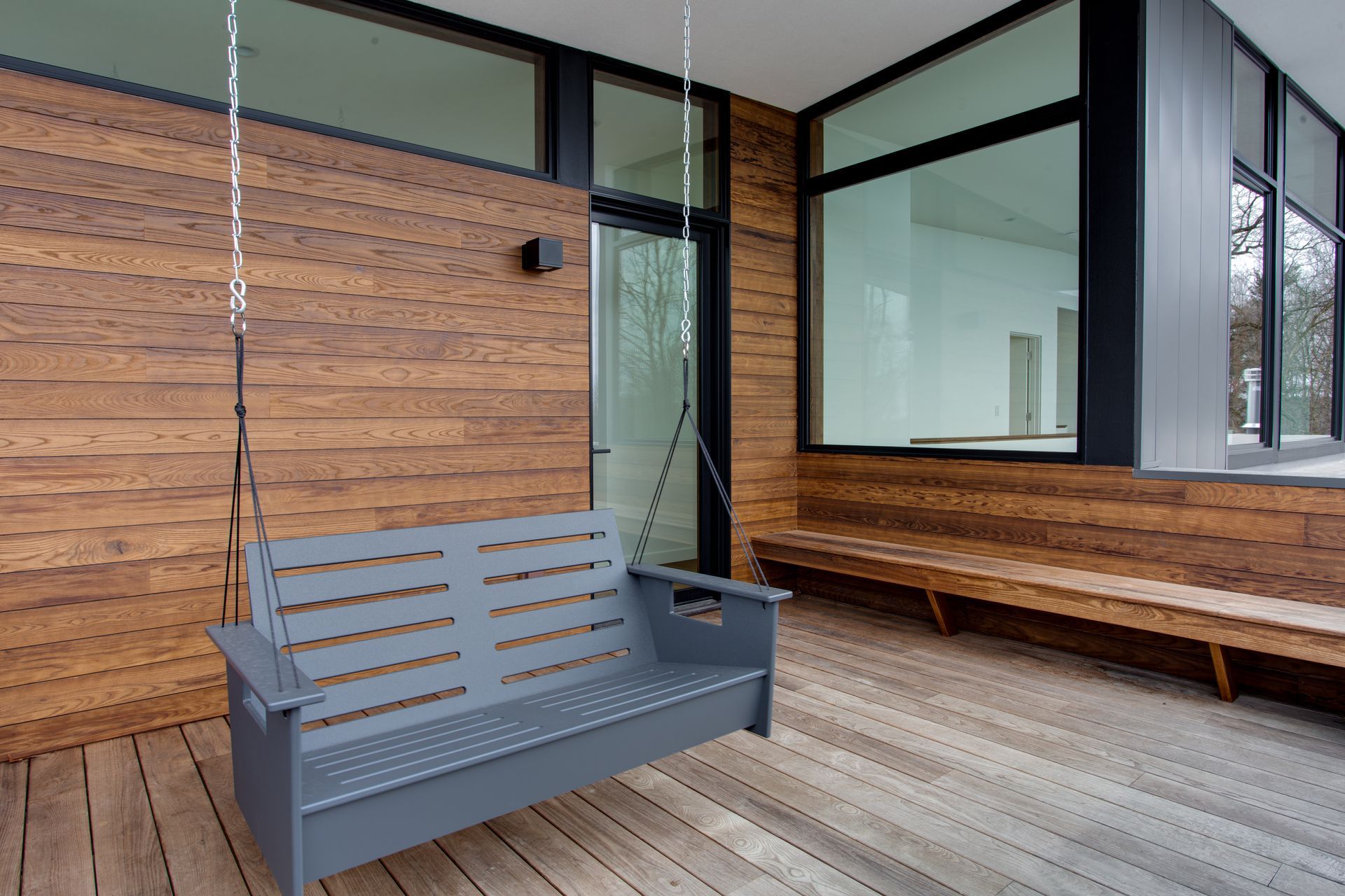Modern patio with gray bench, wood-paneled wall, and large windows beside a house