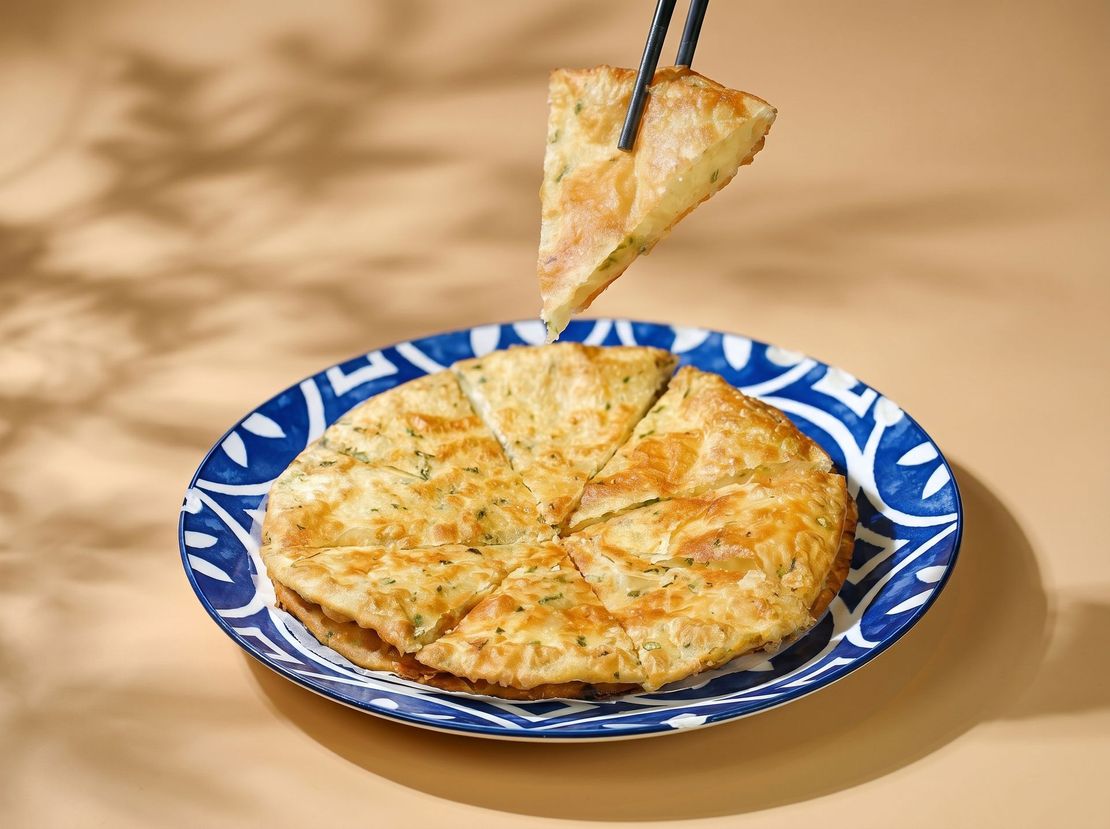 Slice of cheese pizza lifted from a blue patterned plate on a tan tablecloth