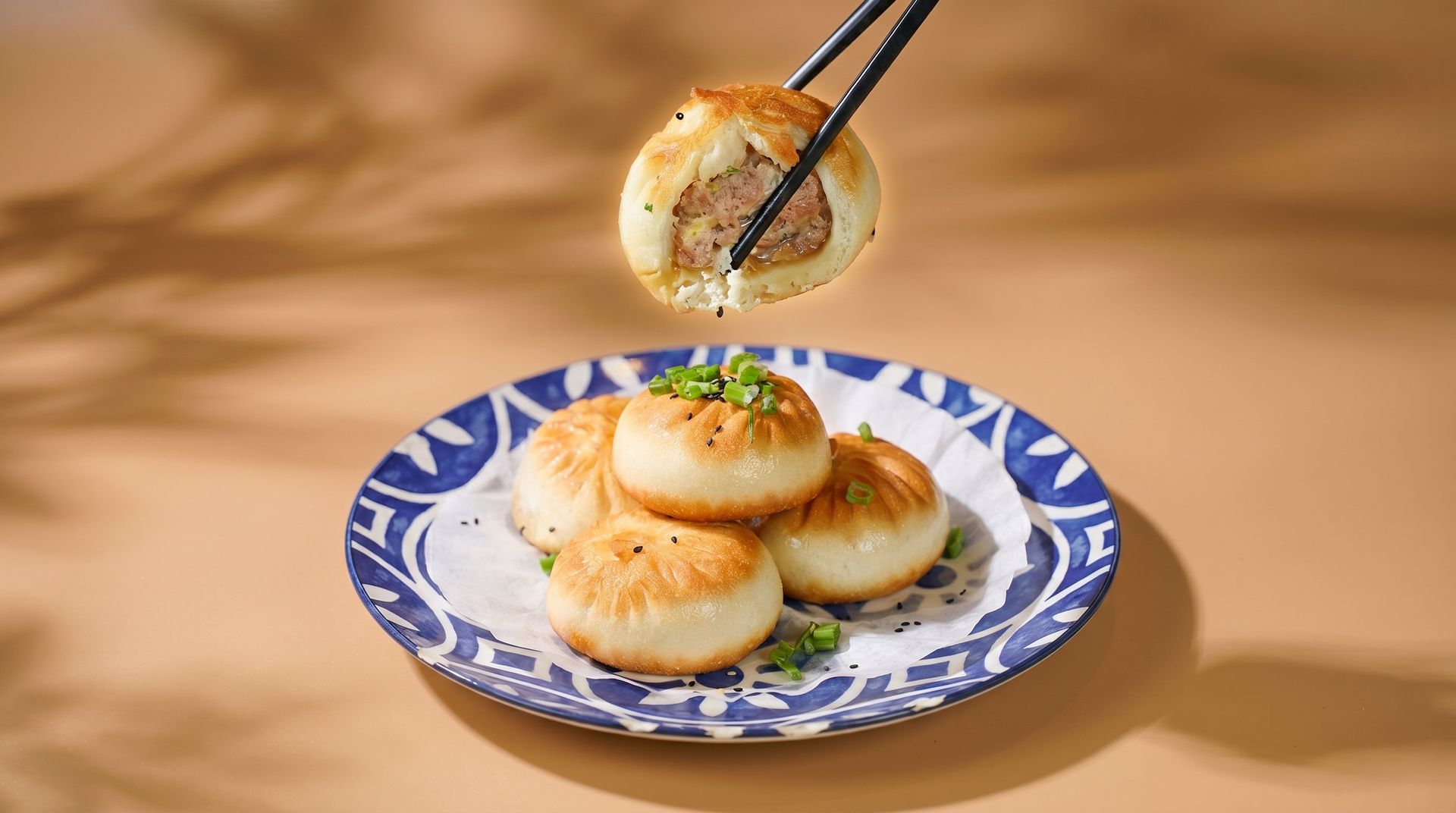 Chopsticks lifting a sesame dumpling from a blue patterned plate with three dumplings on a tan tablecloth