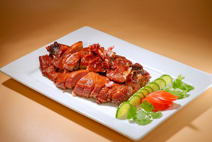A spoon lifts spicy tofu cubes from a bowl of saucy tofu garnished with chopped herbs.