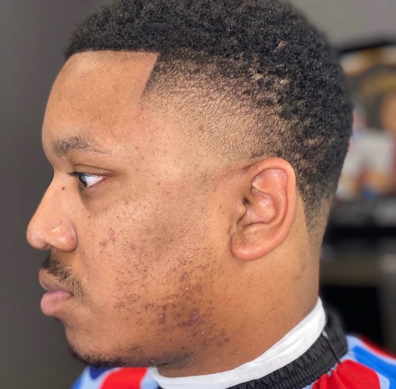 A side profile of a person with a fresh, sharp-lined fade haircut and a short, neatly trimmed mustache.