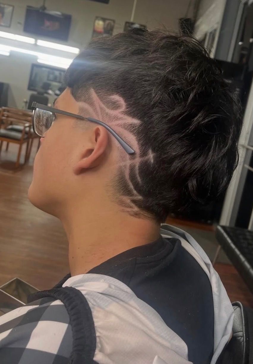 Profile view of a haircut featuring a shaved side with an intricate tribal-style design and dark, textured hair on top.