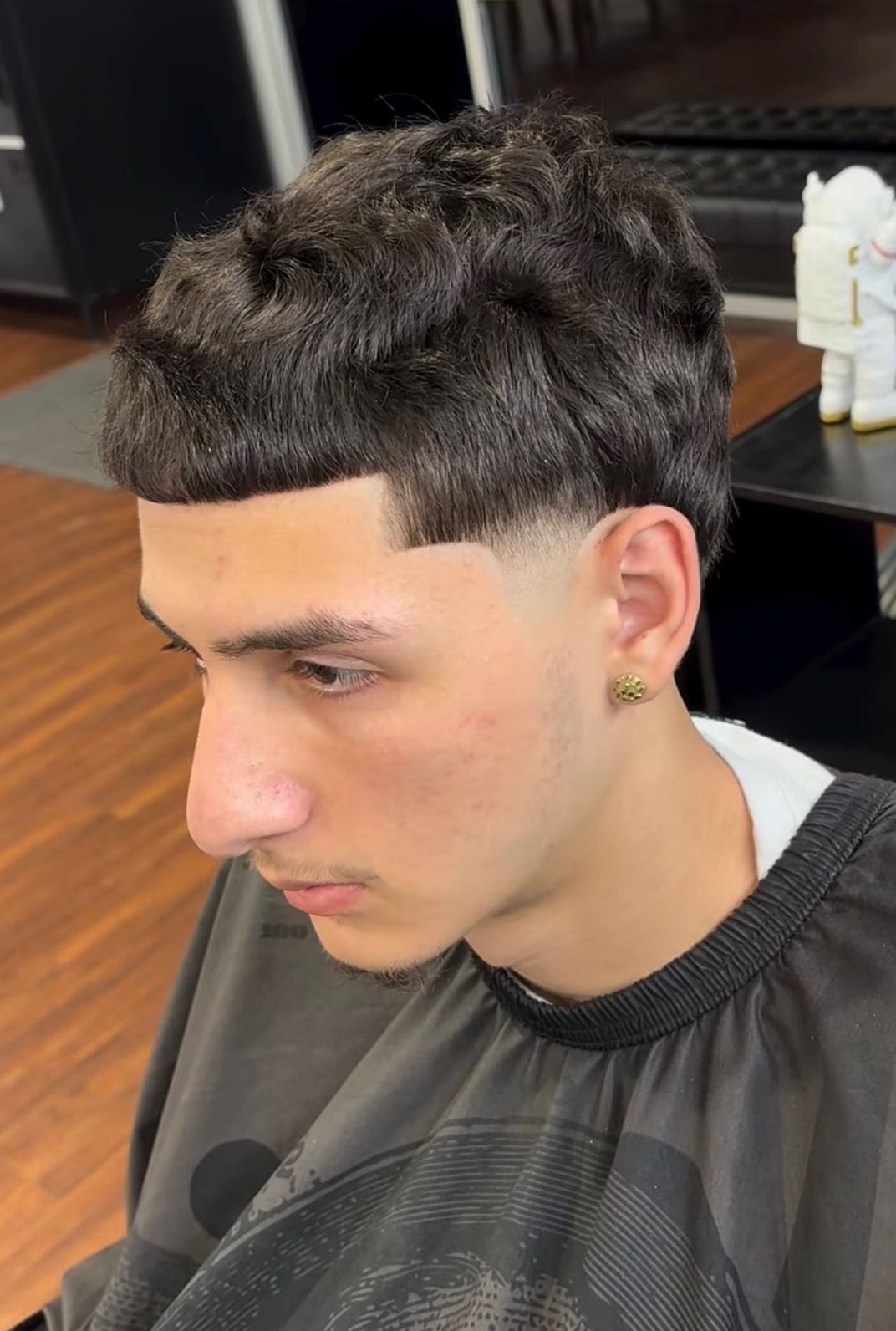 A close-up view of a person with a textured, layered haircut and a clean skin fade on the side, seen in a barber shop.