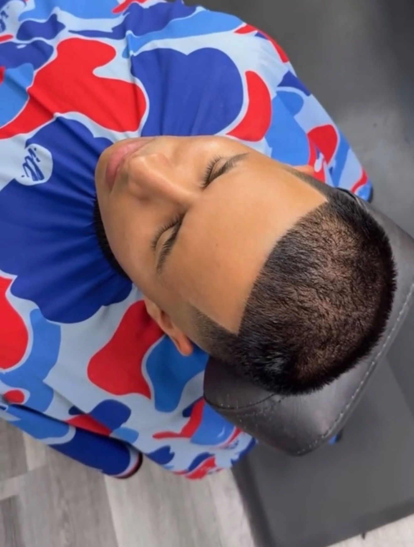 A person in a barber's cape rests in a chair while getting a fresh haircut with a clean line-up.