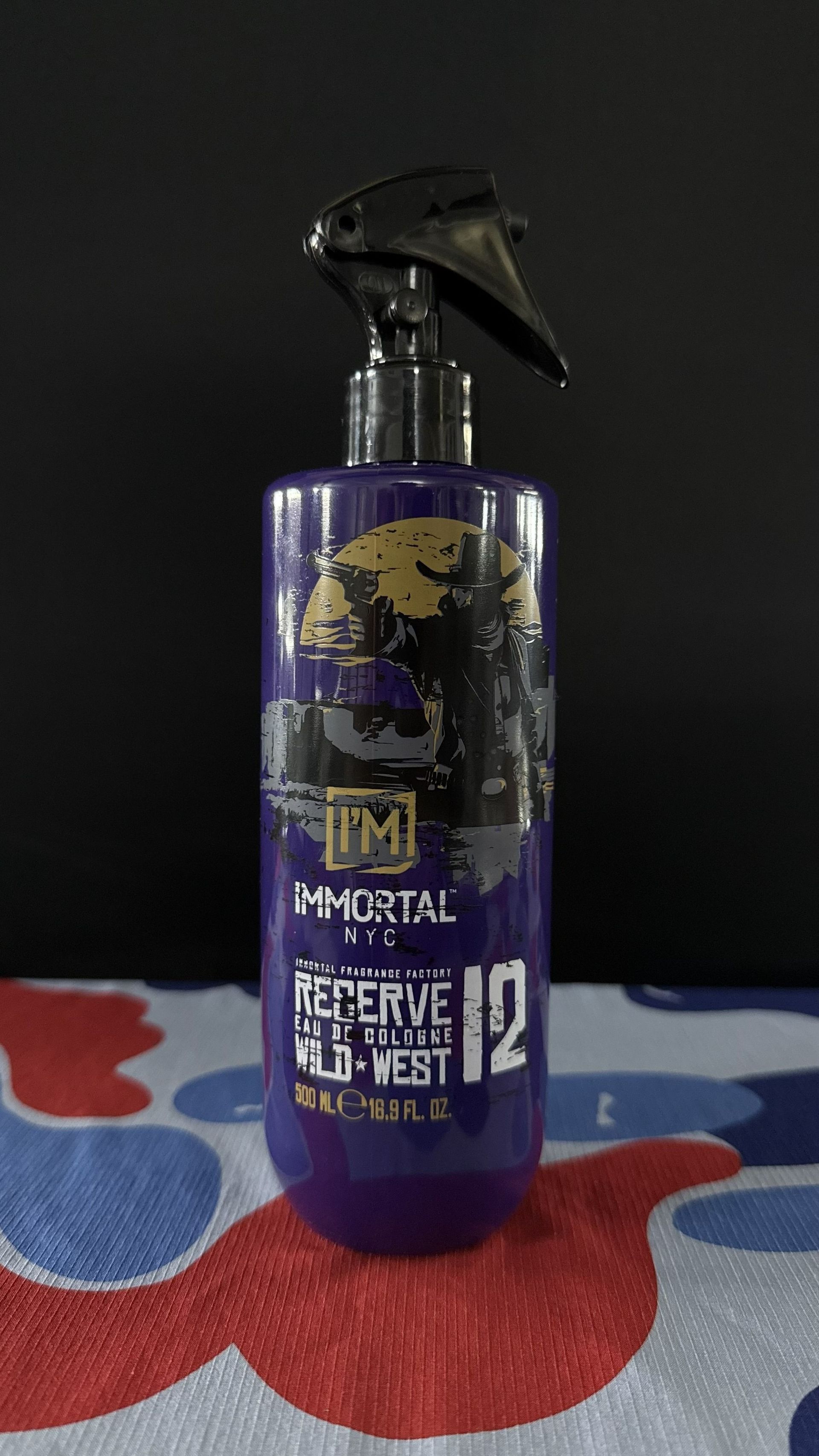 A purple spray bottle of Immortal NYC Reserve Wild Vest hair styling product stands on a red and blue patterned surface.