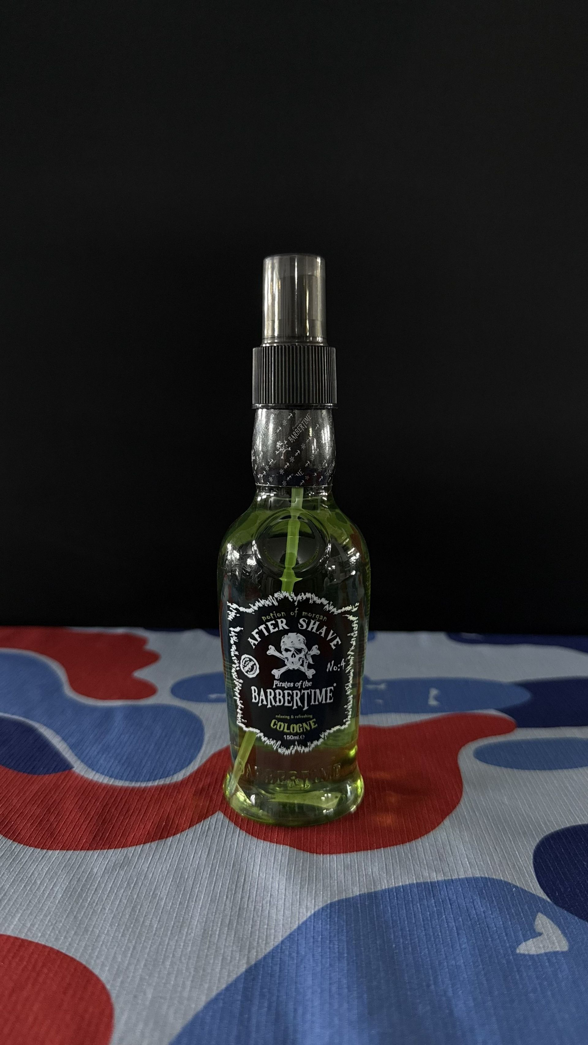 A small, clear glass spray bottle filled with pale yellow liquid, featuring a black label with a skull and crossbones.