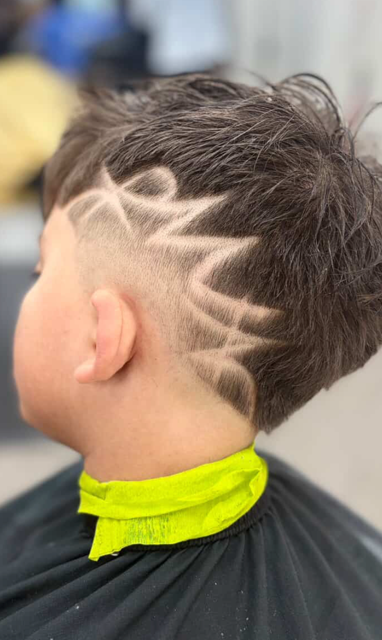 A close-up of a haircut featuring a fade on the side of the head with a detailed, zig-zag geometric hair design.