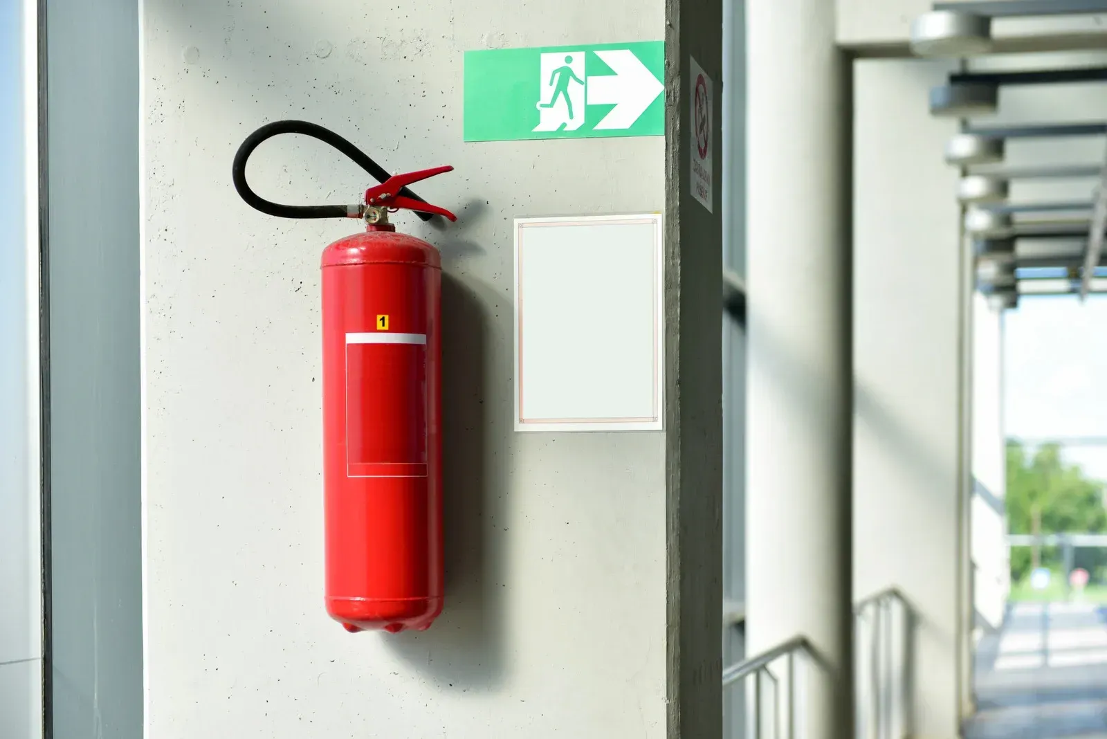 Red fire extinguisher mounted on a white wall with an exit sign.