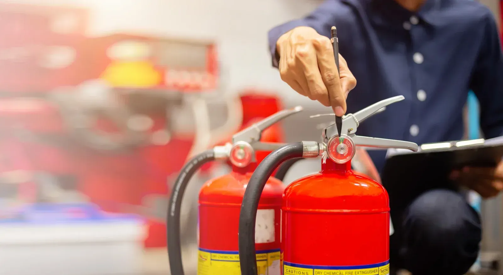 Person inspecting red fire extinguishers with a clipboard.