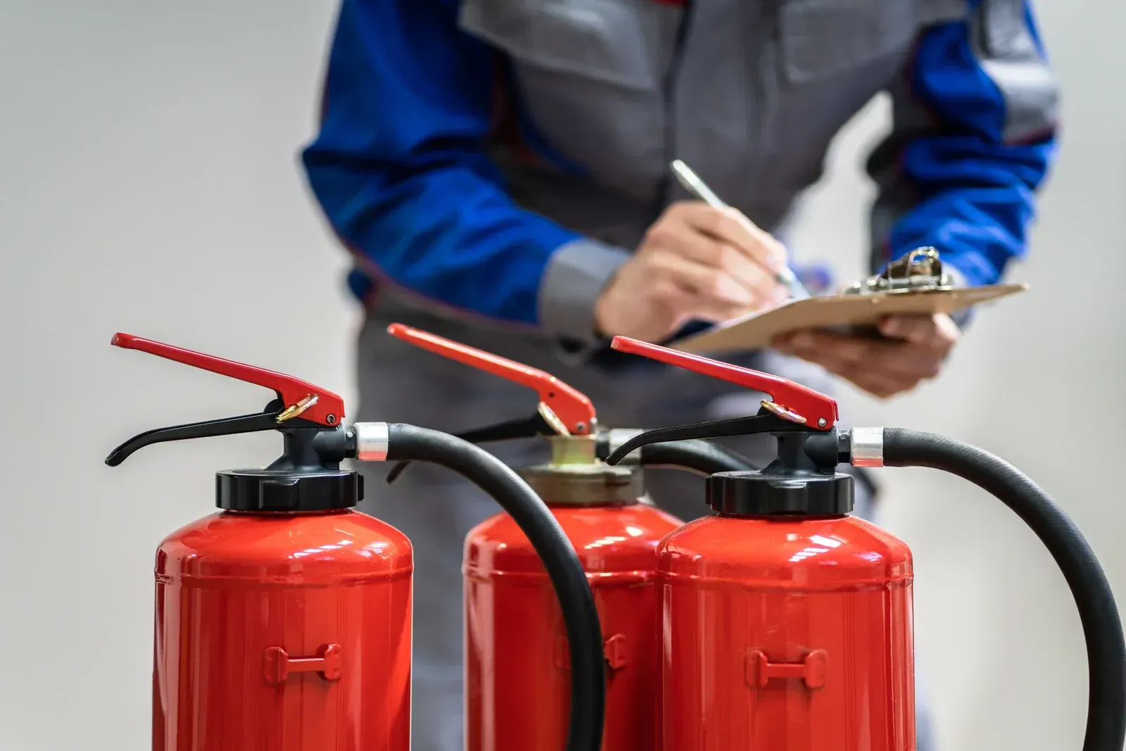 Fire extinguishers in a row, being inspected by a person in work uniform, writing on a clipboard.