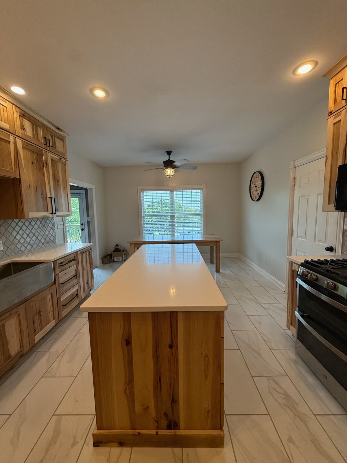 Bright kitchen with wood cabinets, central island, tiled floor, and window at the far end.