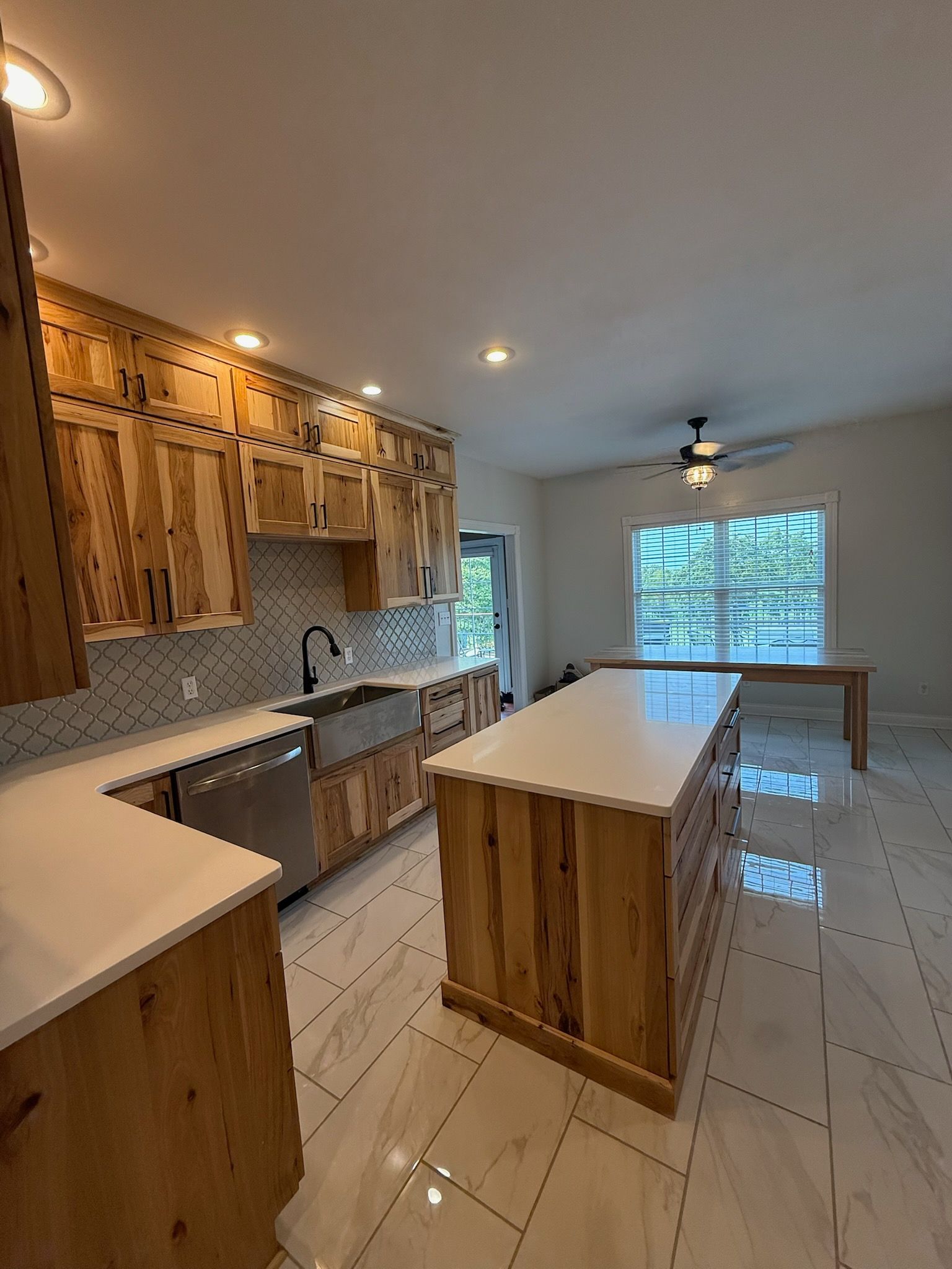 Modern kitchen with wood cabinets, white island, glossy tile floor, and large window overlooking greenery