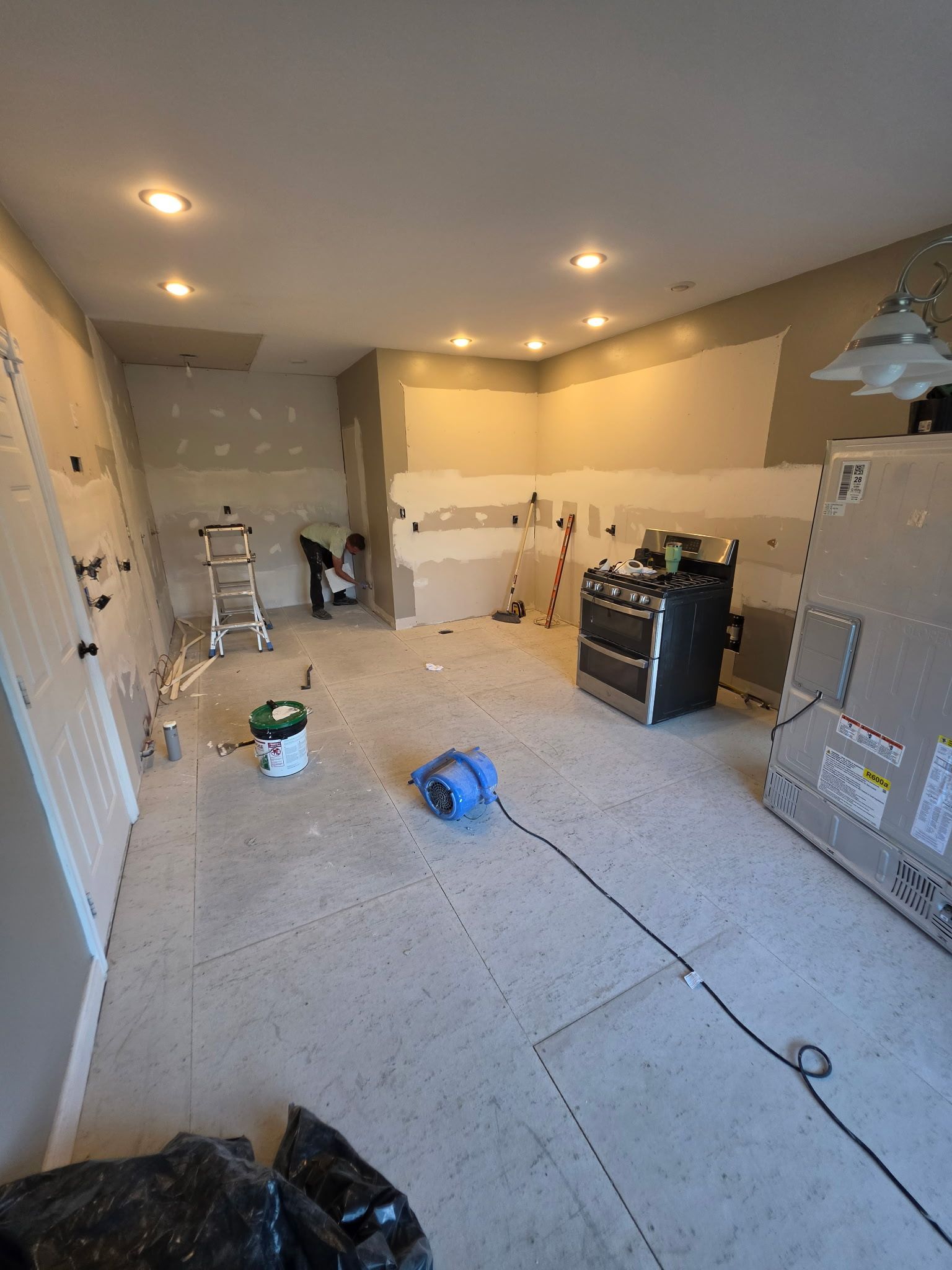 Unfinished garage interior with drywall tools, paint buckets, and a ladder under recessed ceiling lights