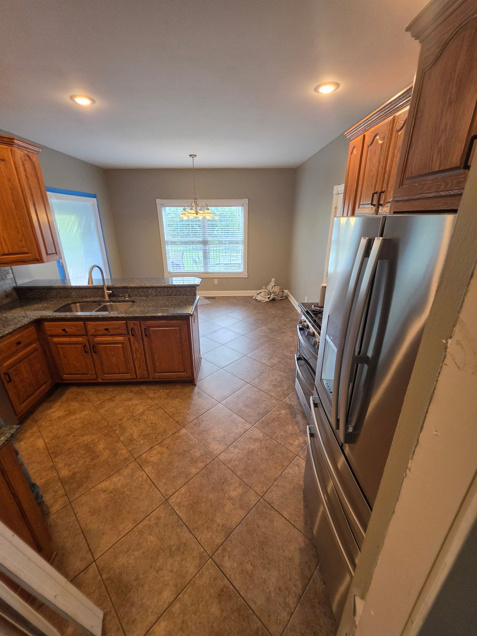 Bright kitchen with wooden cabinets, stainless steel appliances, tiled floor, and a window at the back.