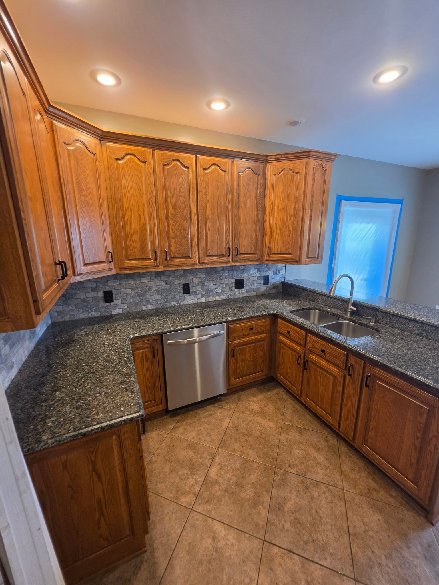U-shaped kitchen with wood cabinets, granite counters, stainless dishwasher, and recessed ceiling lights.