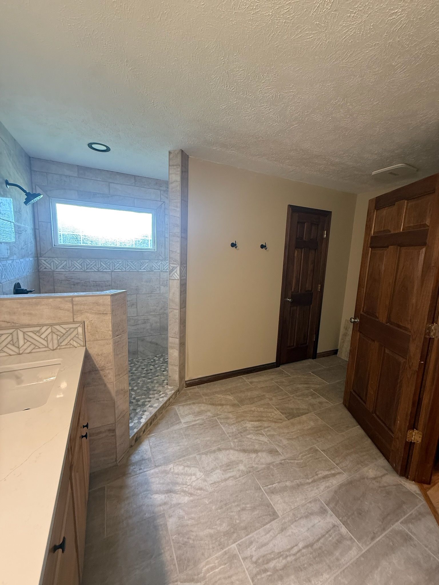 Small tiled bathroom with walk-in shower, wood vanity, and wooden doors.