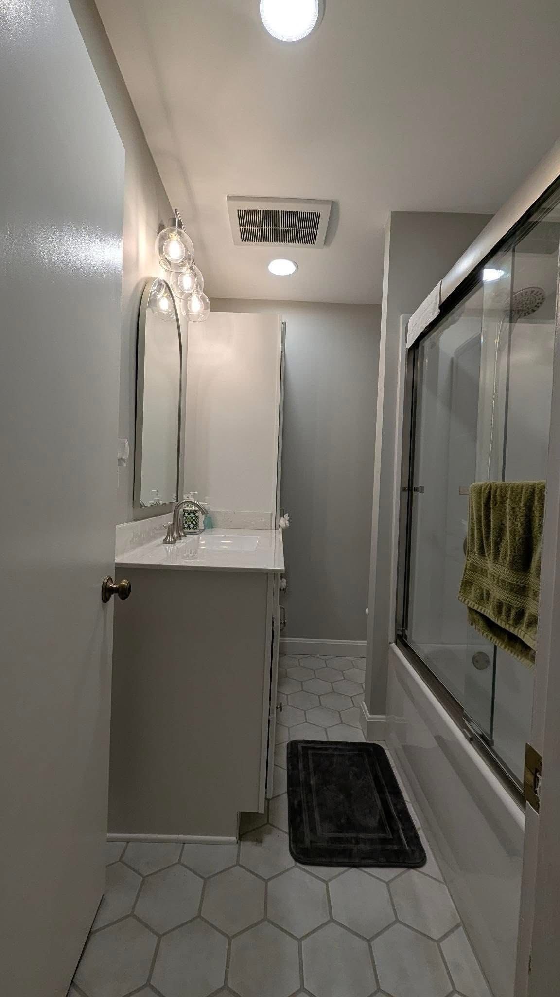 Spacious bathroom with green walls, white tile, vanity sinks, mirrors, and a chandelier ceiling light
