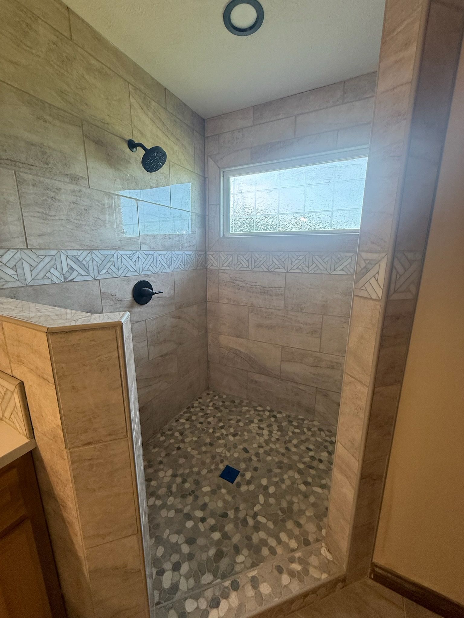 Walk-in tiled shower with mosaic floor, wall niche, and two black fixtures.