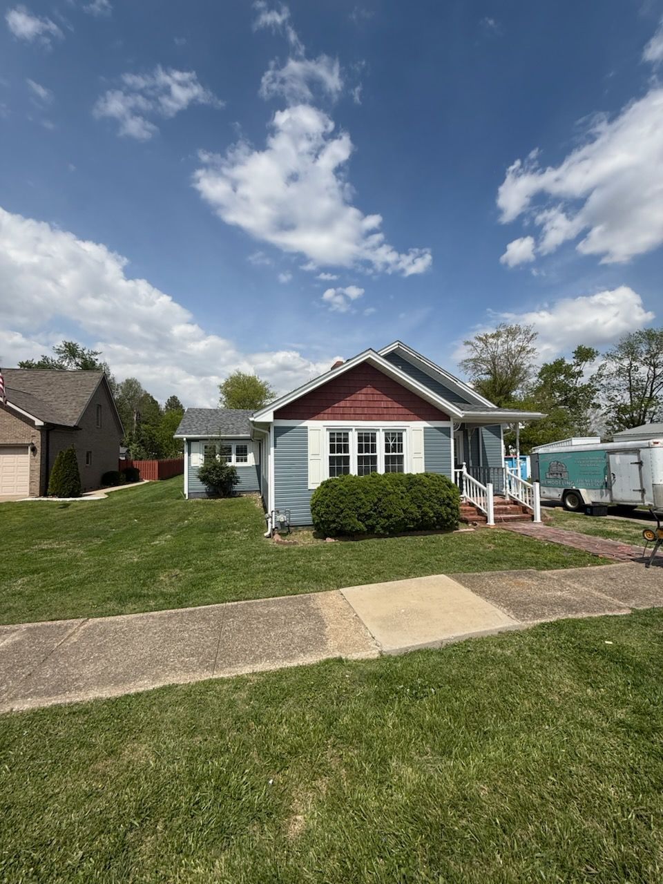 Small blue house with red gable, white trim, and a front lawn under a partly cloudy sky.