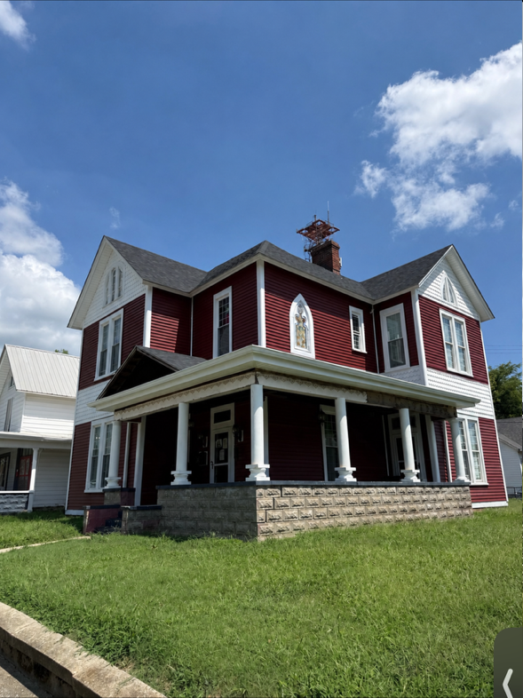 Red Victorian-style house with white trim and a front porch under a blue sky