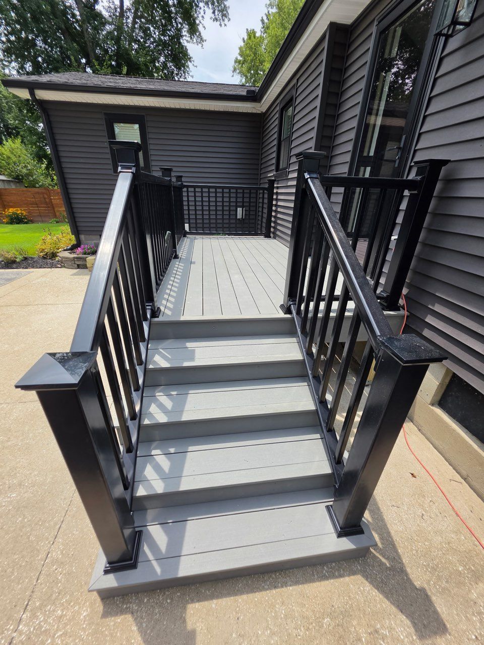 Front steps with gray stairs, black railings, and a landing beside a house.