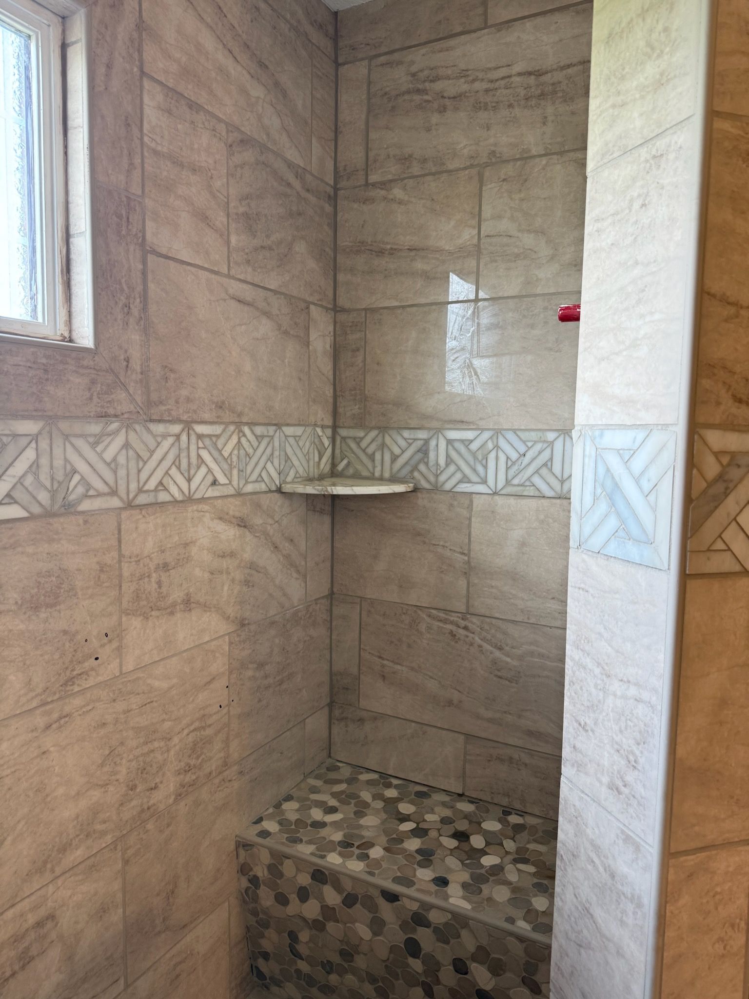 Stone-tiled shower stall with a mosaic floor and a small window.