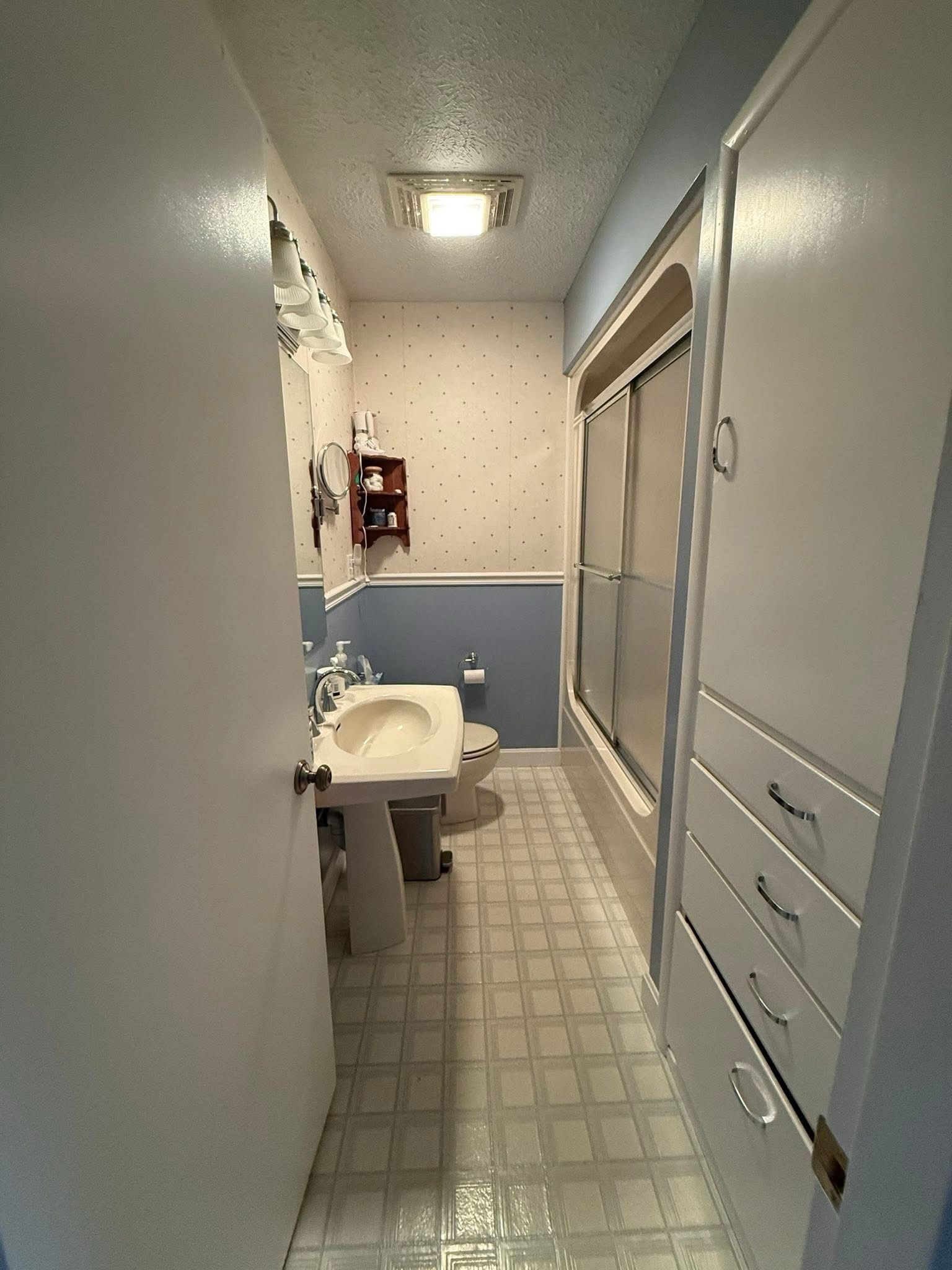 Narrow bathroom hallway with sink, toilet, blue lower walls, and large mirror cabinet.
