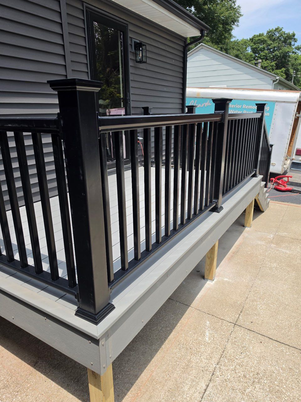 Black porch railing on a gray house with a small front deck and driveway beside it