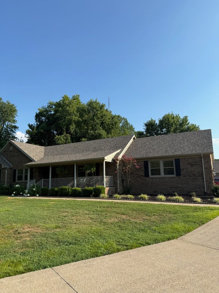 Single-story brick house with a front porch, green lawn, and clear blue sky