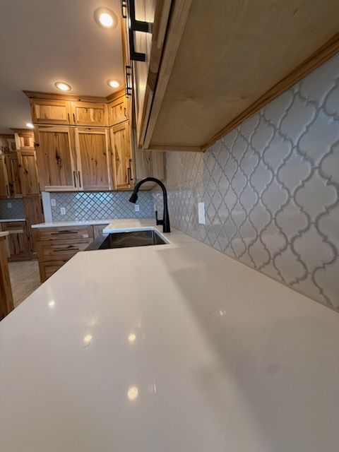 Modern kitchen with white island, wooden cabinets, patterned backsplash, and black faucet lighting