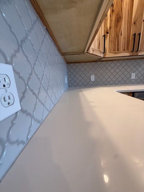 Kitchen countertop with marble-pattern backsplash, white outlets, and wood cabinets under a slanted ceiling